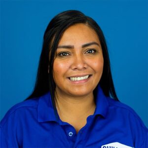 Woman with long black hair wearing a blue collared shirt, smiling in front of a plain blue background.
