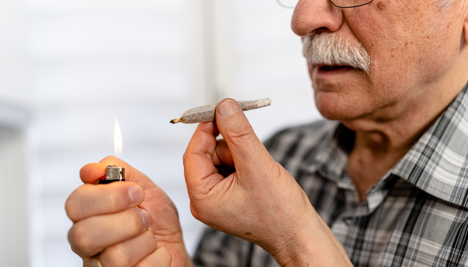 An older man holds a lighter in one hand and a rolled cigarette in the other, preparing to light it.