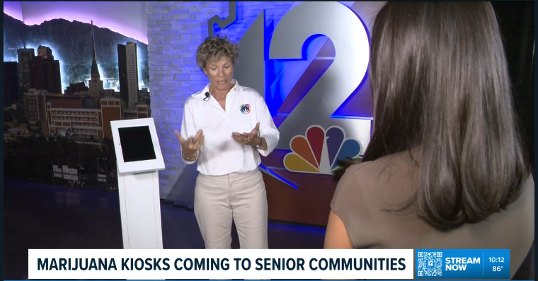 Two women converse in a TV studio; one stands near a kiosk. The screen headline reads, "Marijuana kiosks coming to senior communities.